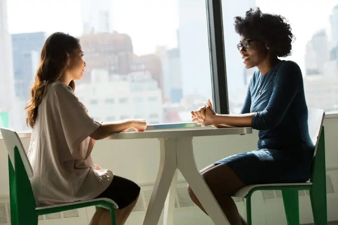 Dos mujeres sentadas al lado de una mesa y hablando.